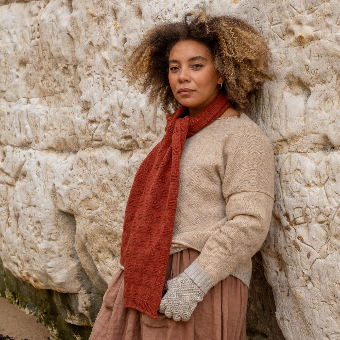 A rust-colored textured knit scarf draped around a woman's neck.  The scarf features a subtle grid pattern.