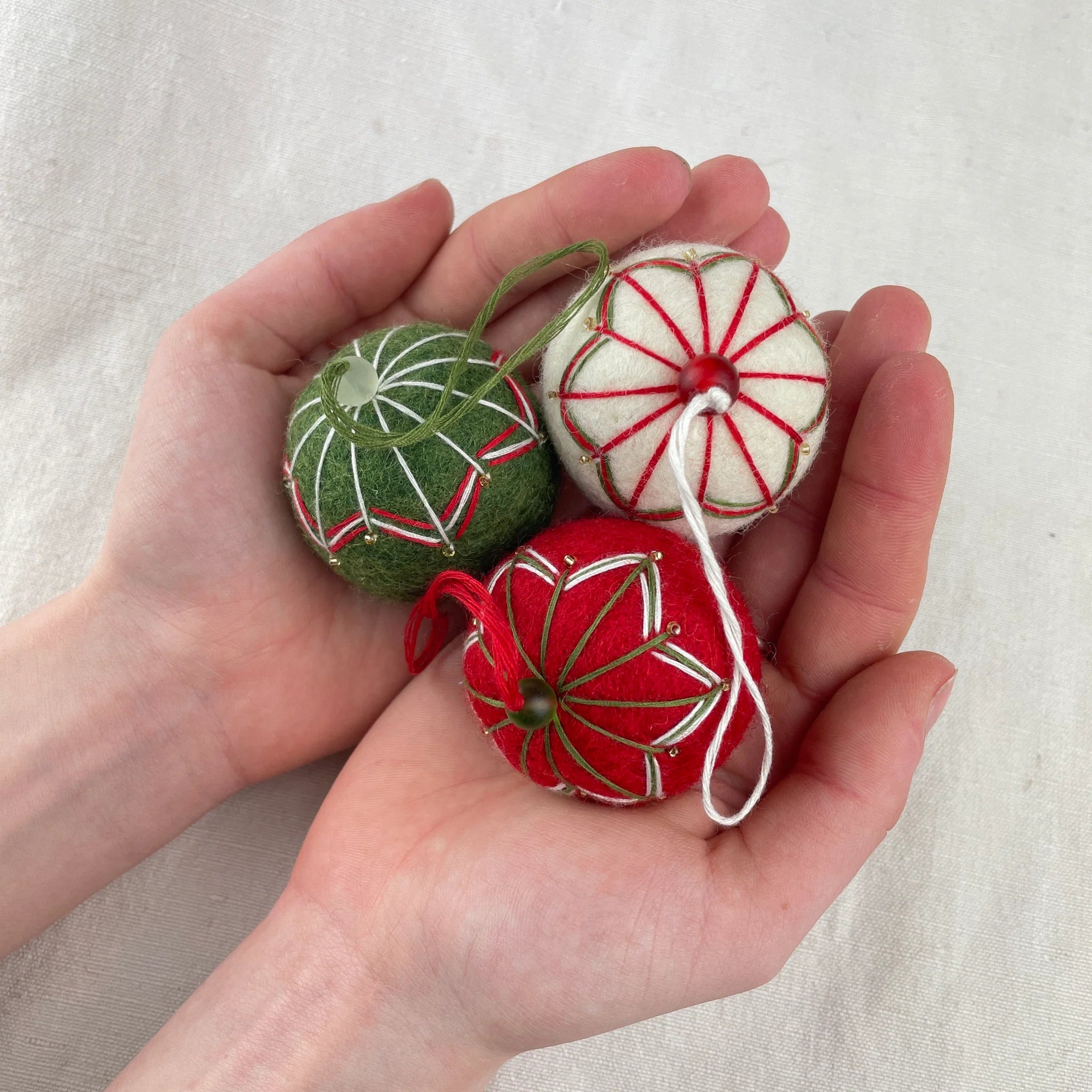 Three handmade felt Christmas ornaments in red, green, and white.