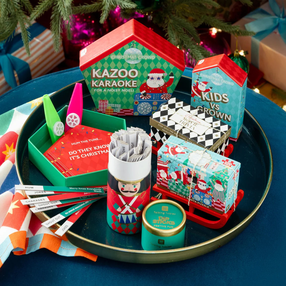 Assorted Christmas-themed games and toys on a tray with festive decorations in the background.