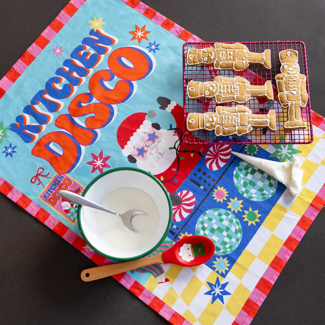 Colorful kitchen mat with 'Kitchen Disco' text, robot-shaped cookies, and baking tools on a dark surface.