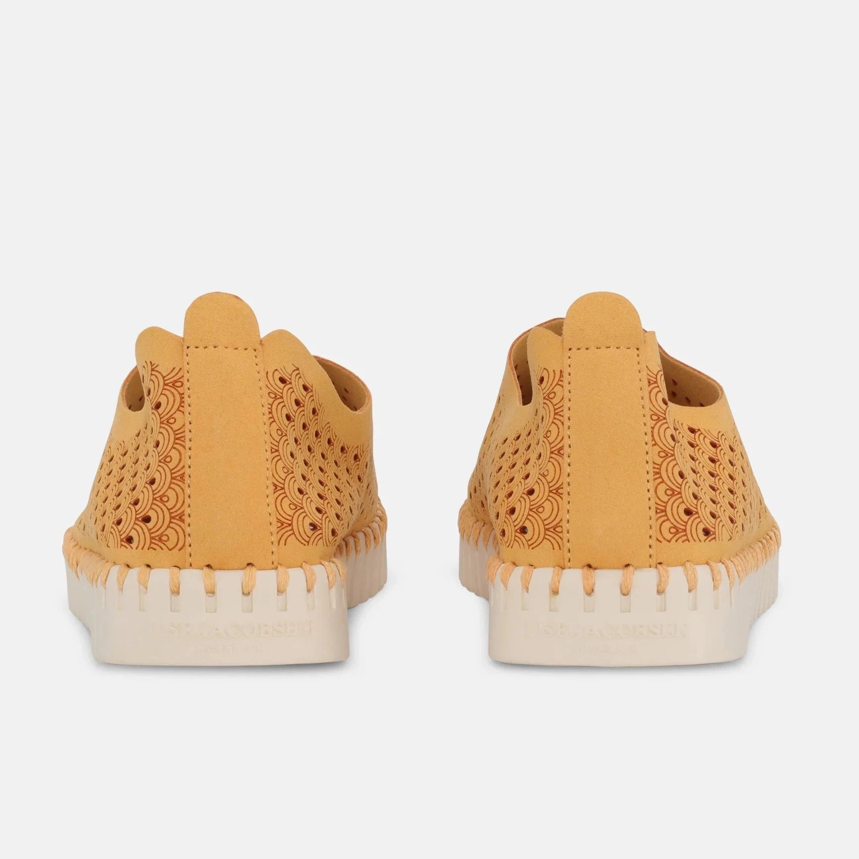 Pair of mustard-yellow slip-on shoes with intricate cutout pattern and off-white sole. The design features a repeating wave