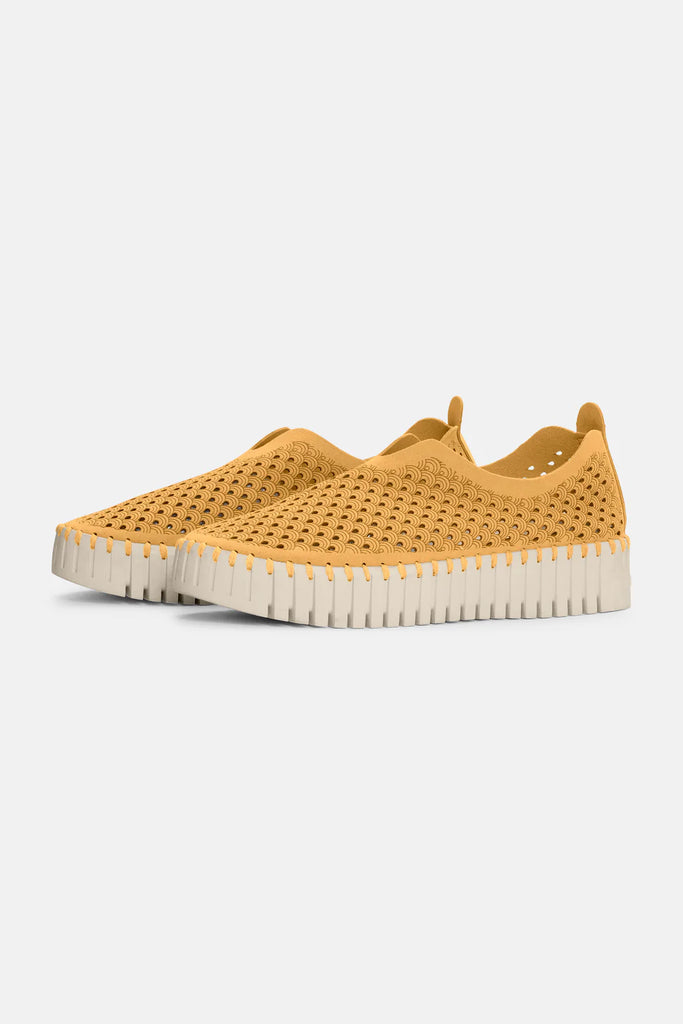 Mustard yellow slip-on shoes with a textured, perforated upper and off-white, scalloped sole.
