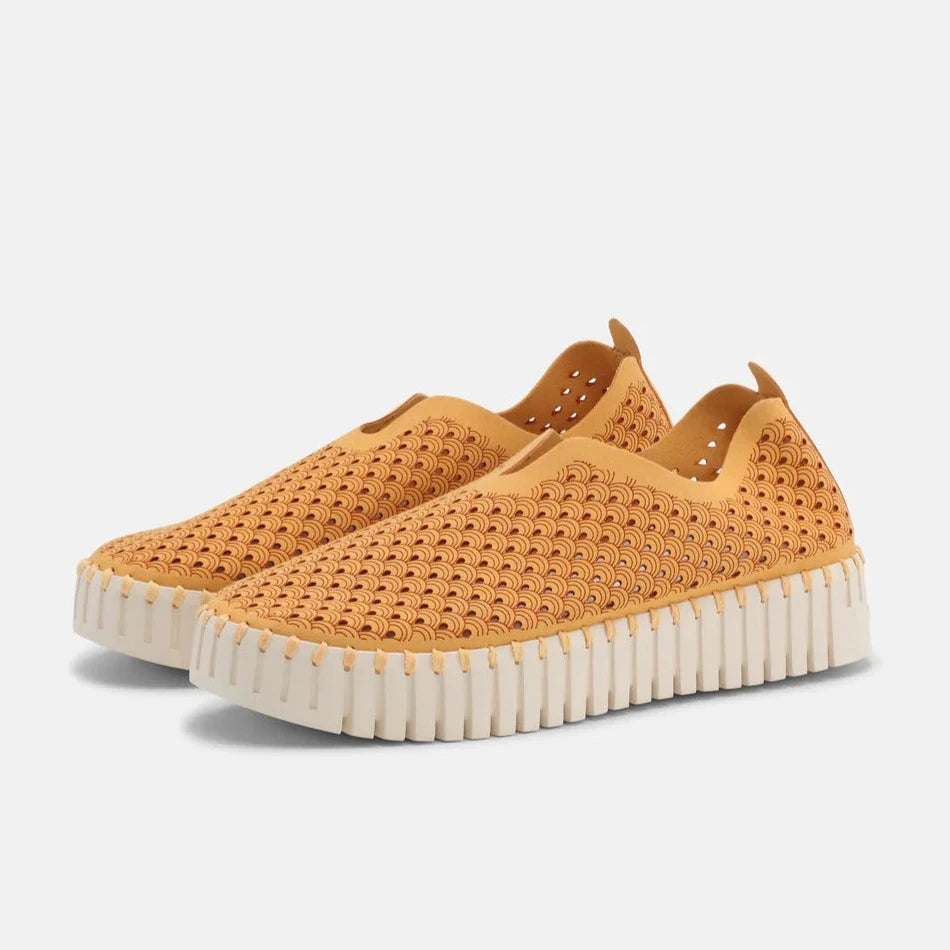 Mustard yellow slip-on shoes with a textured, perforated pattern and a cream-colored, scalloped sole.