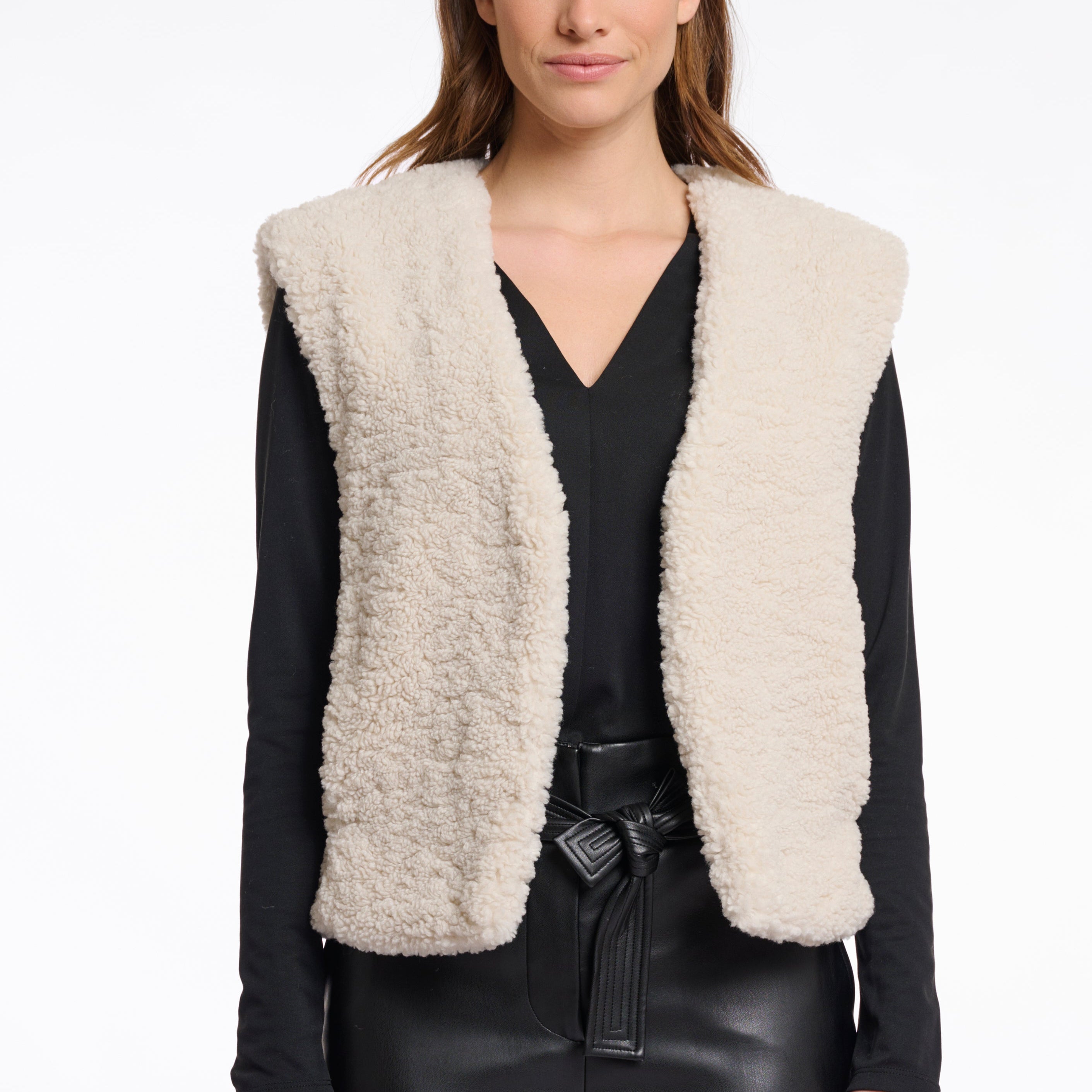 Woman wearing a cream sherpa vest over a black outfit on a white background