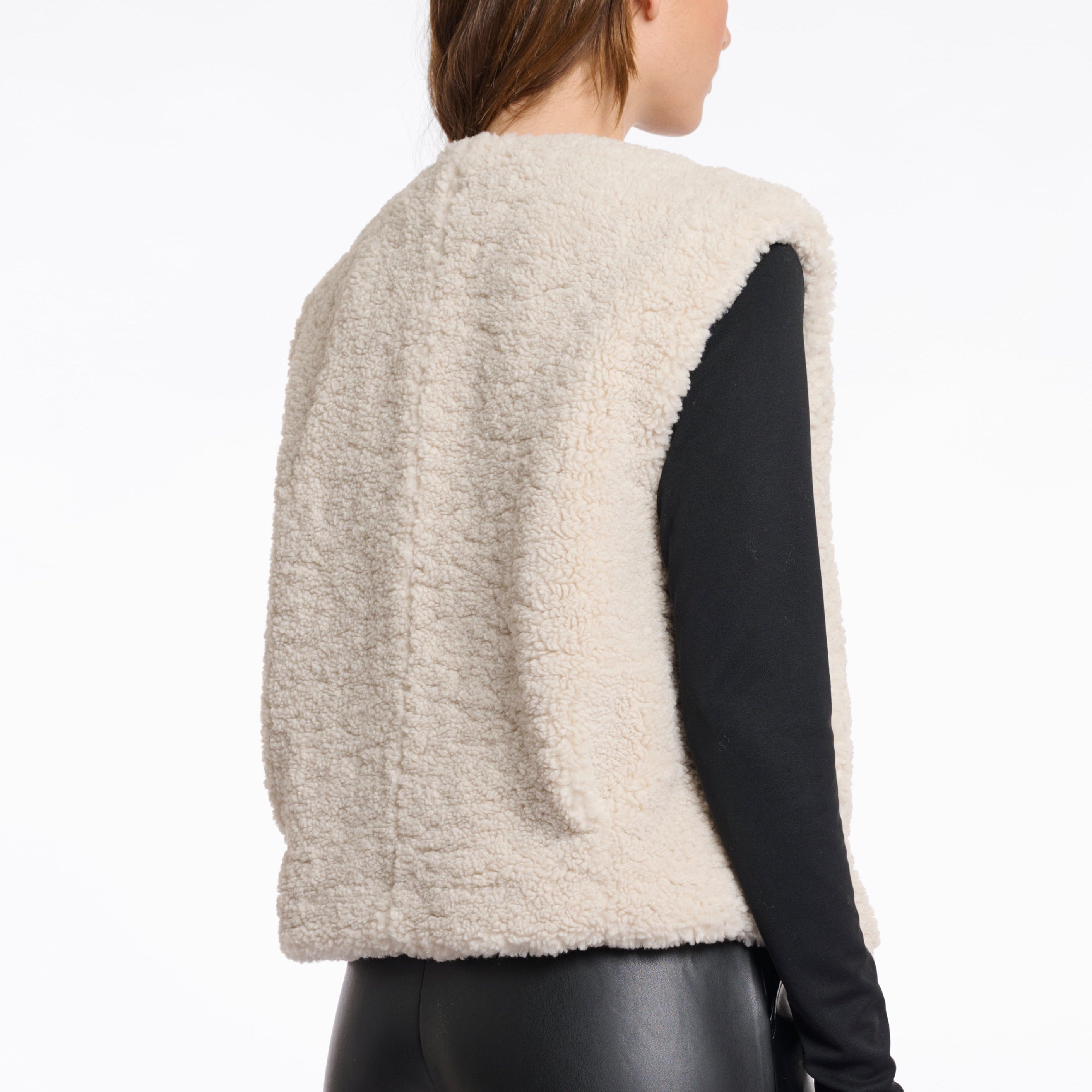 Person wearing a beige fleece vest on a white background