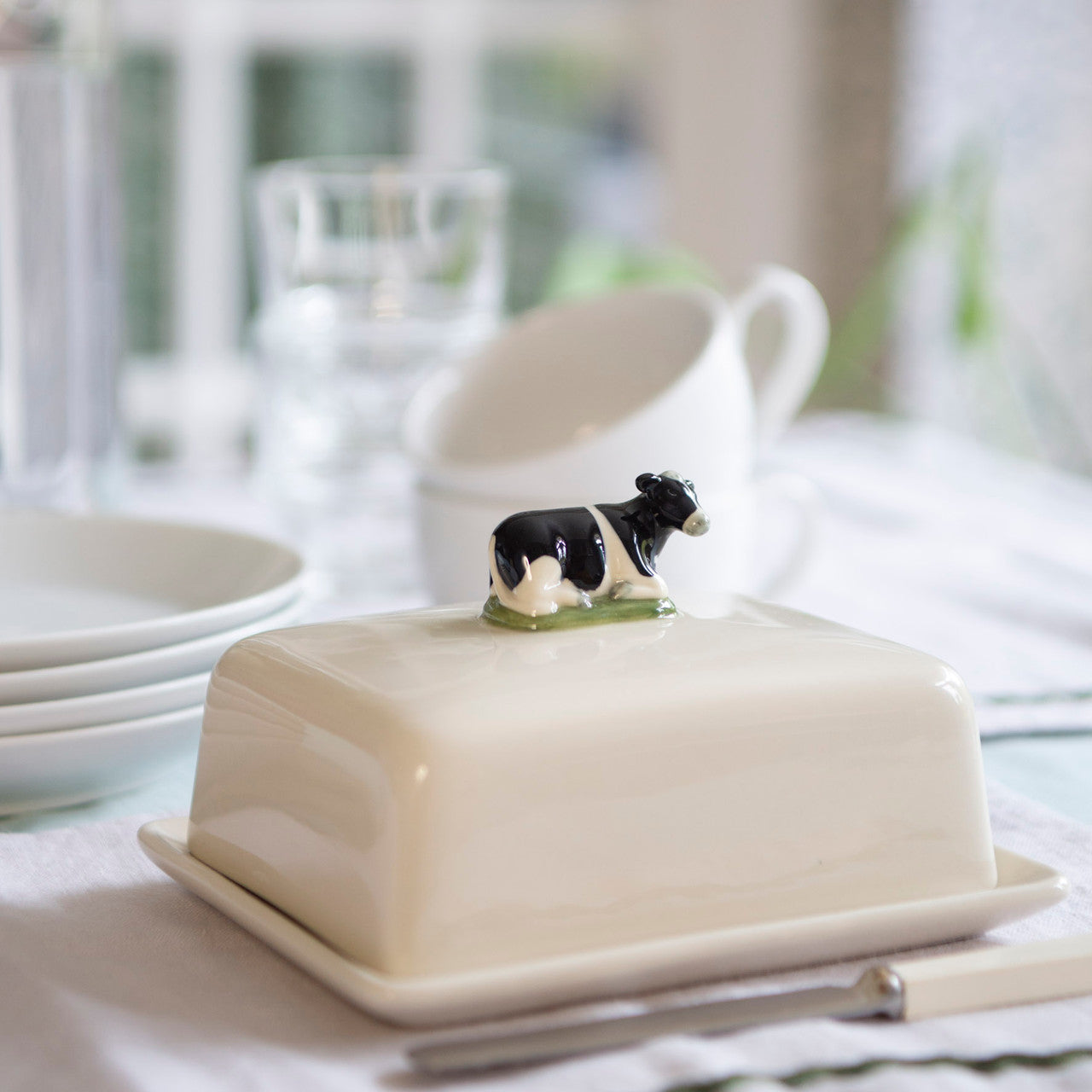 Cream-colored ceramic butter dish with a small black and white cow figurine on top.