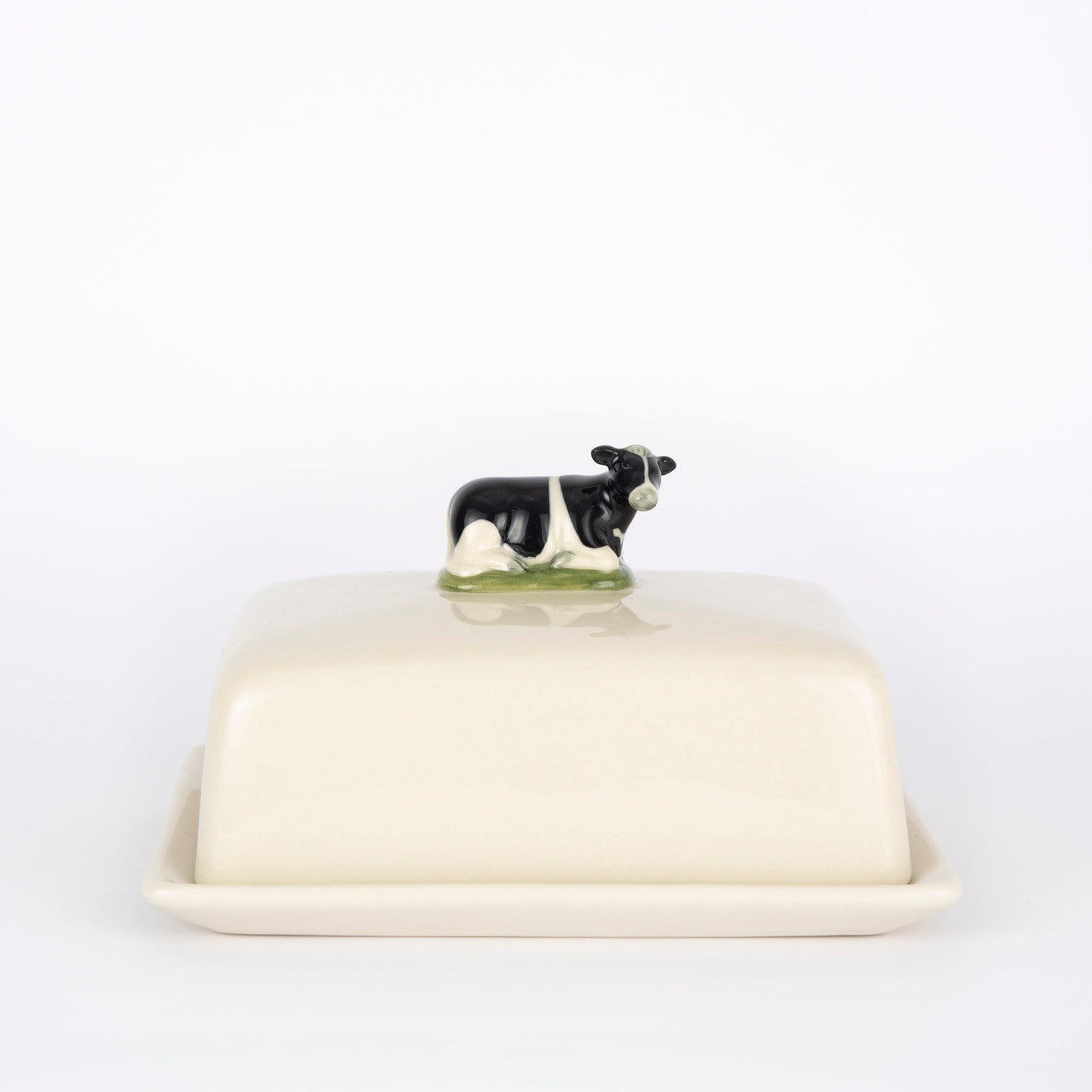 Cream-colored ceramic butter dish with a small black and white cow figurine on the lid.