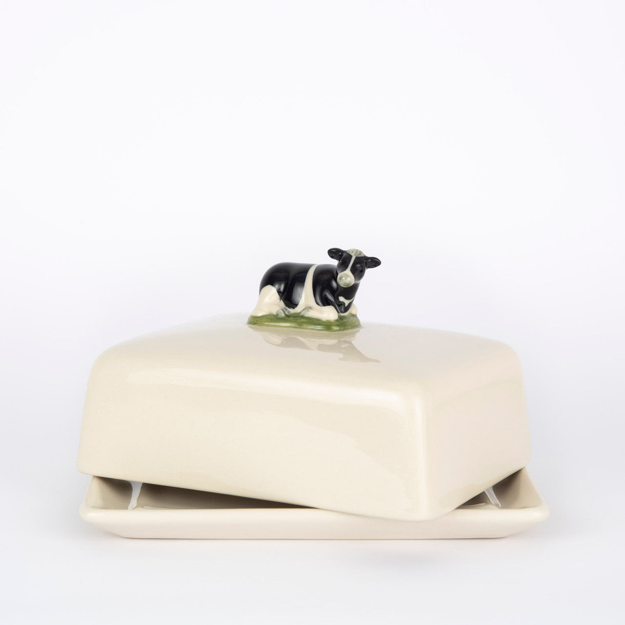 Cream-colored ceramic butter dish with a small black and white cow figurine on the lid.