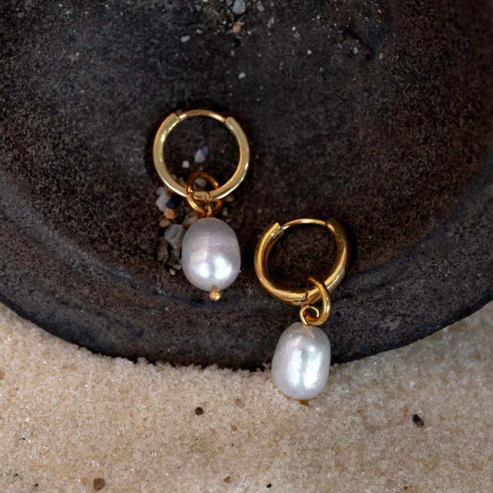 Gold earrings with pearl charms on a textured surface