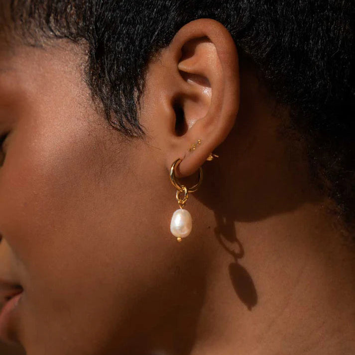 Close-up of an ear wearing a gold hoop earring with a pearl drop.