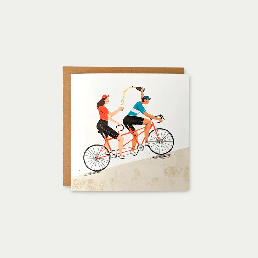 Illustrated greeting card depicting a couple celebrating on a tandem bicycle, pouring champagne.