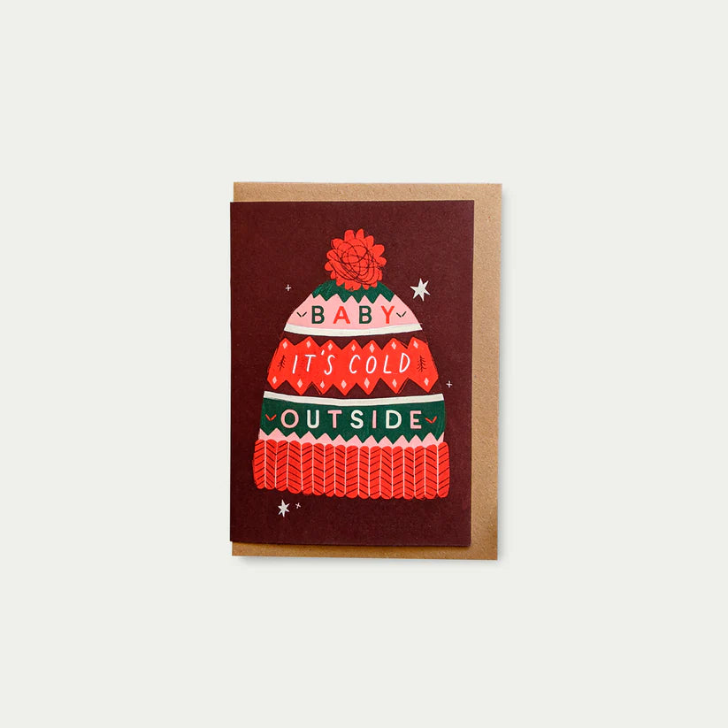 Holiday greeting card featuring a red, green, and pink illustrated winter hat with the text "Baby, It's Cold Outside."