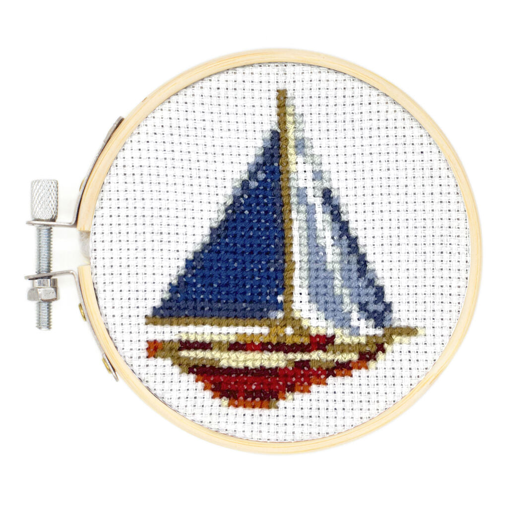 Cross-stitch sailboat artwork in a wooden embroidery hoop.  The sailboat is predominantly blue and red.