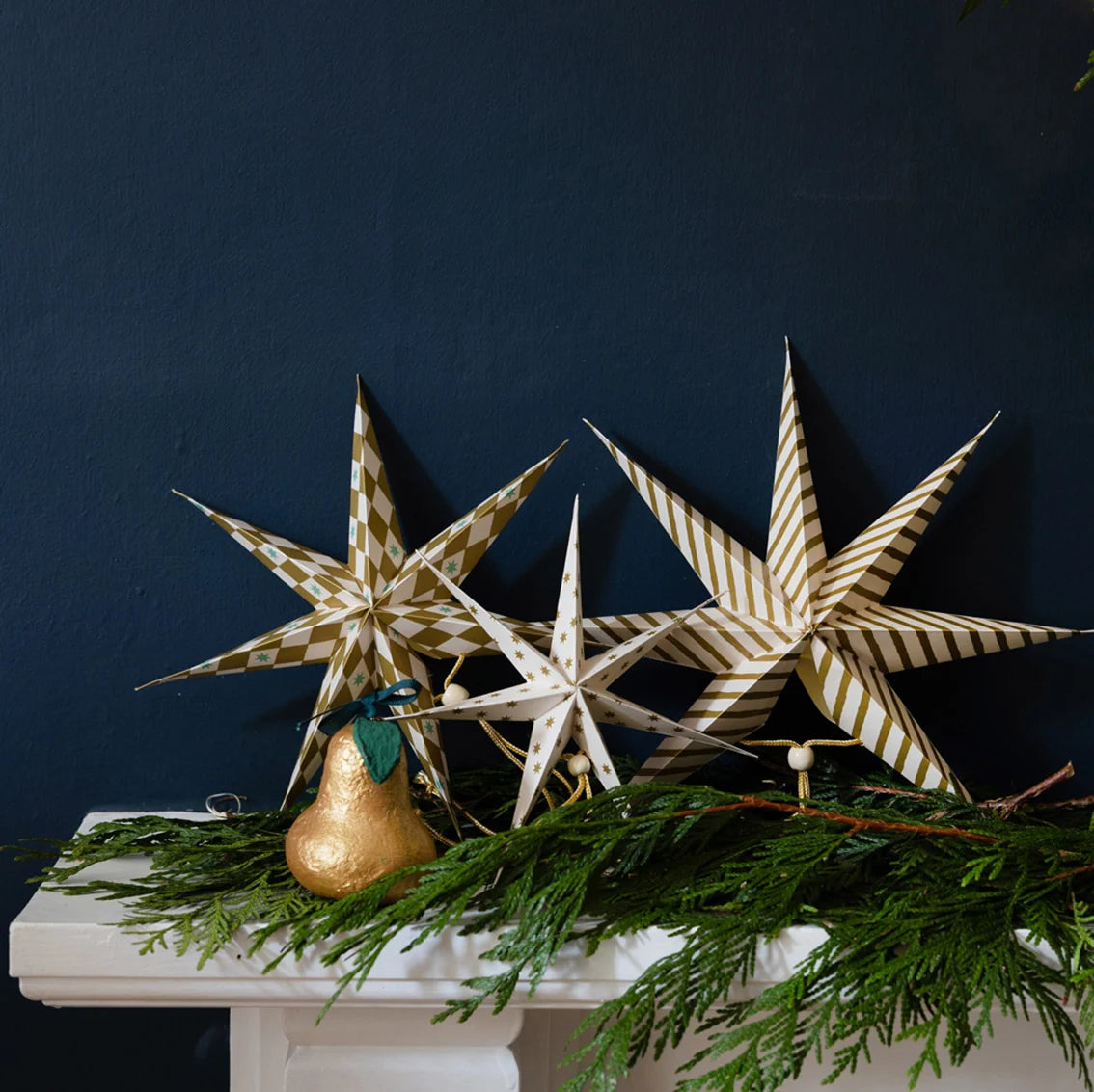 Decorative star-shaped objects and a gold pear on a mantelpiece with a dark blue wall background.
