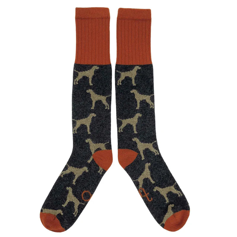 Pair of dark gray crew socks with a repeating pattern of tan dog silhouettes and burnt orange cuffs.