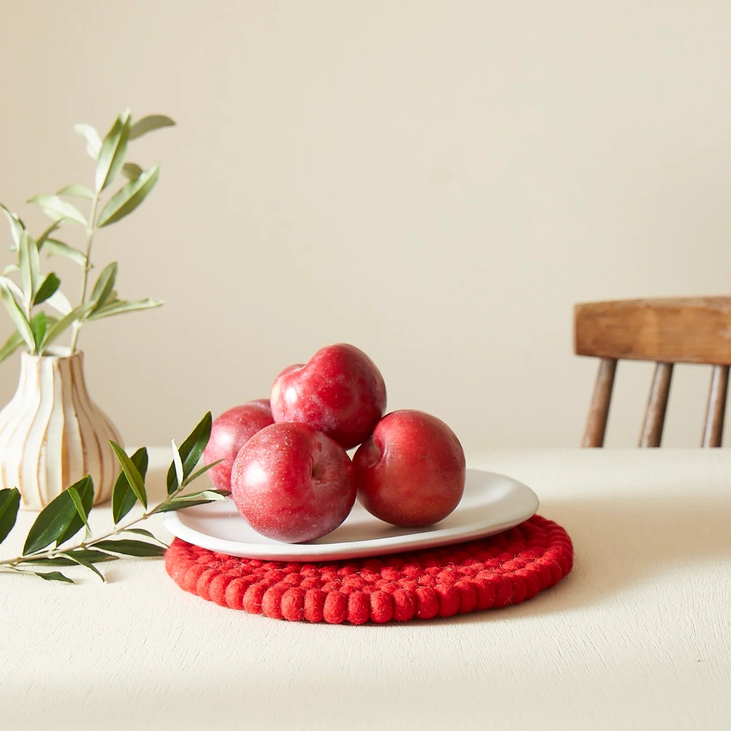 Red plums on a white plate atop a red felt coaster.