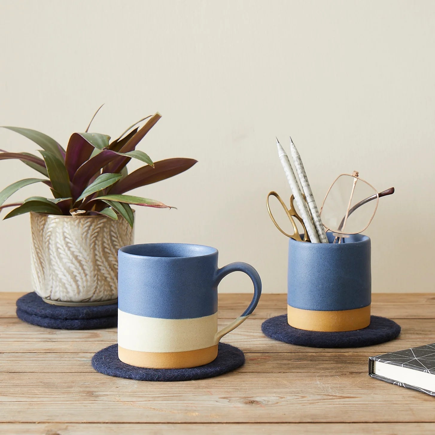 Two-toned blue and cream ceramic mugs with matching pen holders on felt coasters.