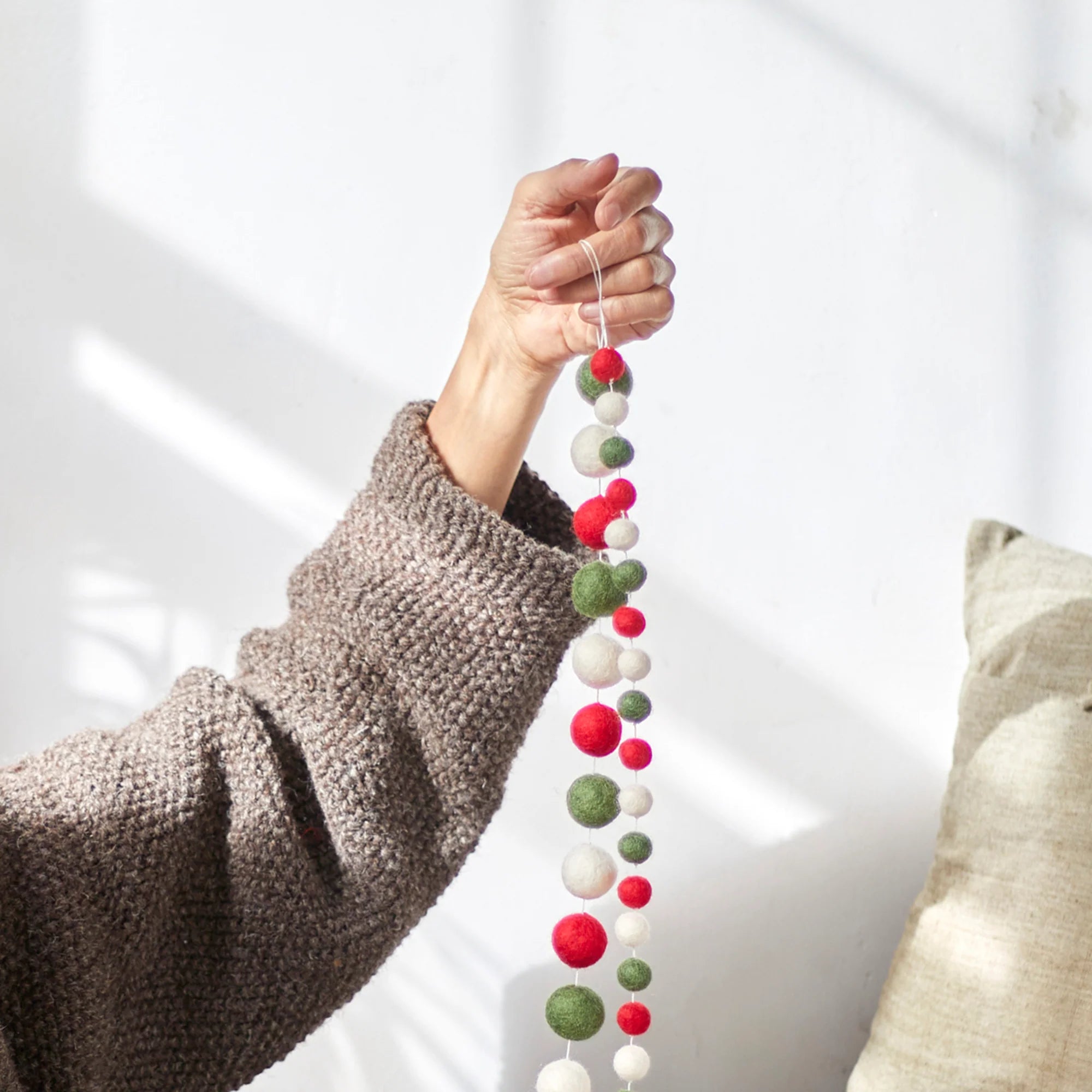 A hand holds a garland of red, green, and white felt balls strung on a white thread.