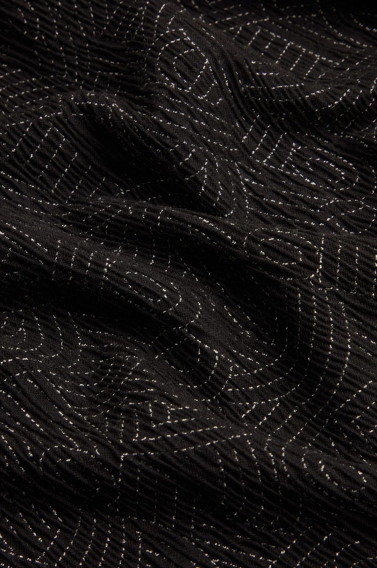A close-up of a black textured fabric with a raised geometric pattern created by contrasting light stitching.