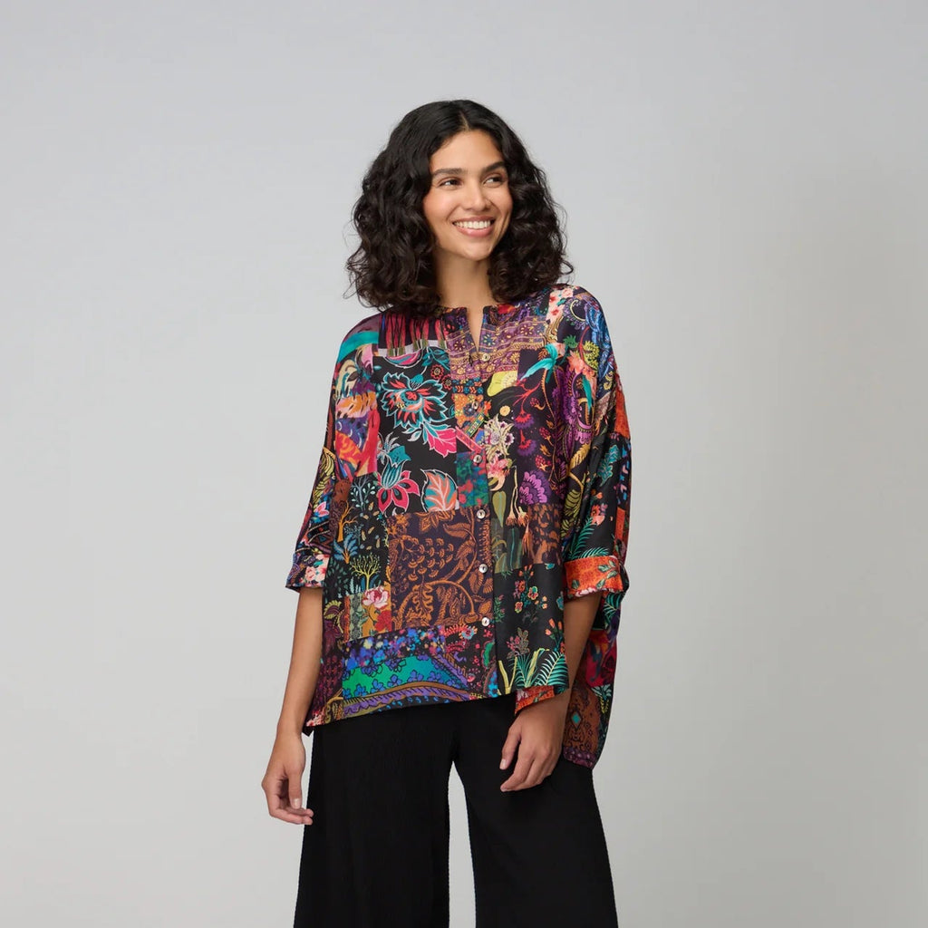 Woman wearing a colorful patterned top and black pants on a white background