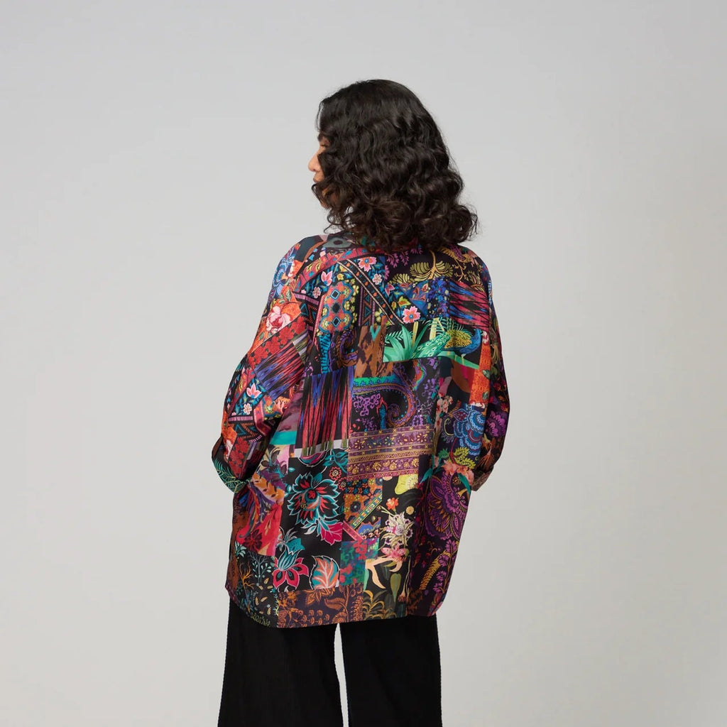 Person wearing a colorful patterned jacket and black pants on a white background