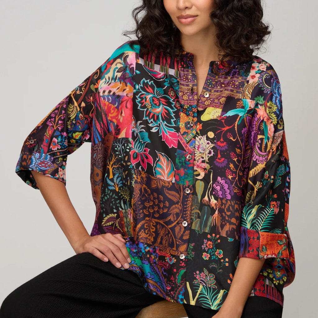 Woman wearing a colorful patterned blouse sitting on a stool against a plain background