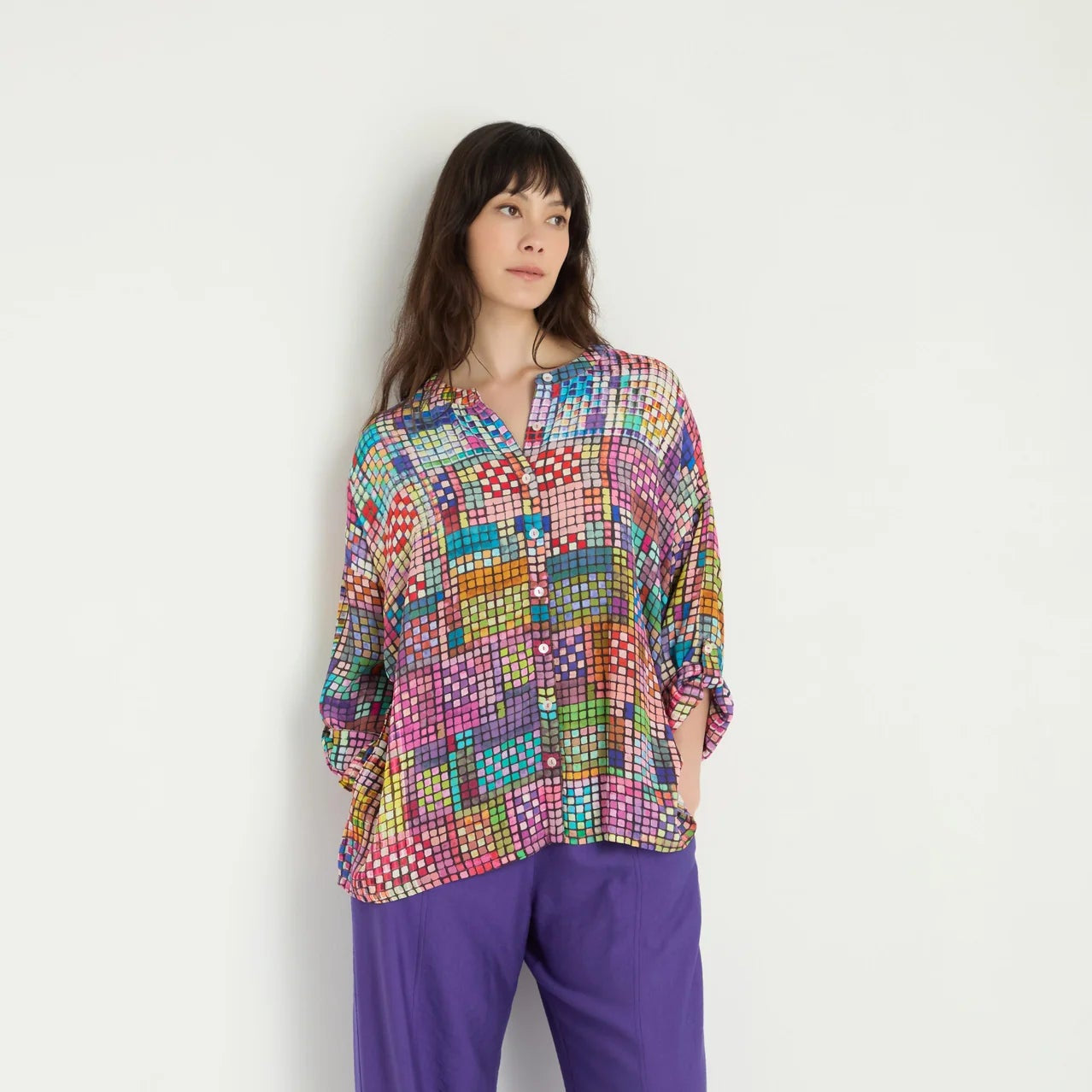 Woman wearing a colorful patterned top and purple pants on a white background