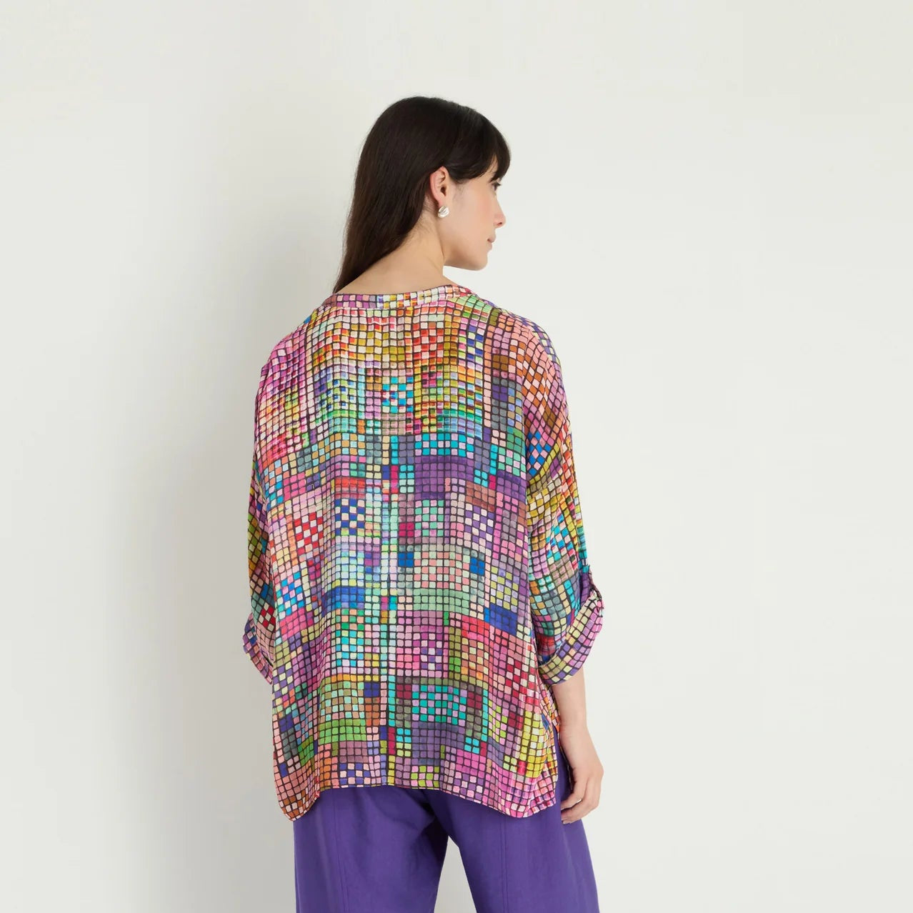 Woman wearing a colorful patterned top and purple pants on a white background