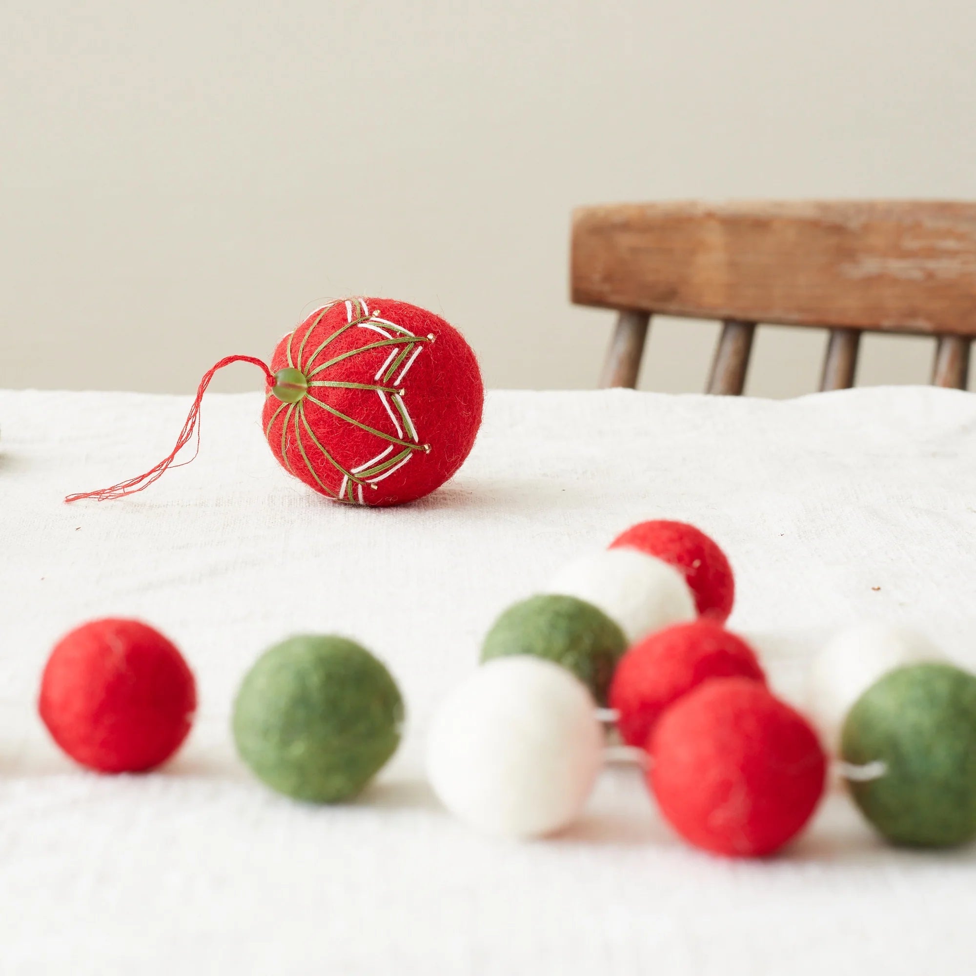Red felt Christmas ornament with green and white embroidery, alongside a garland of red, green, and white felt balls.