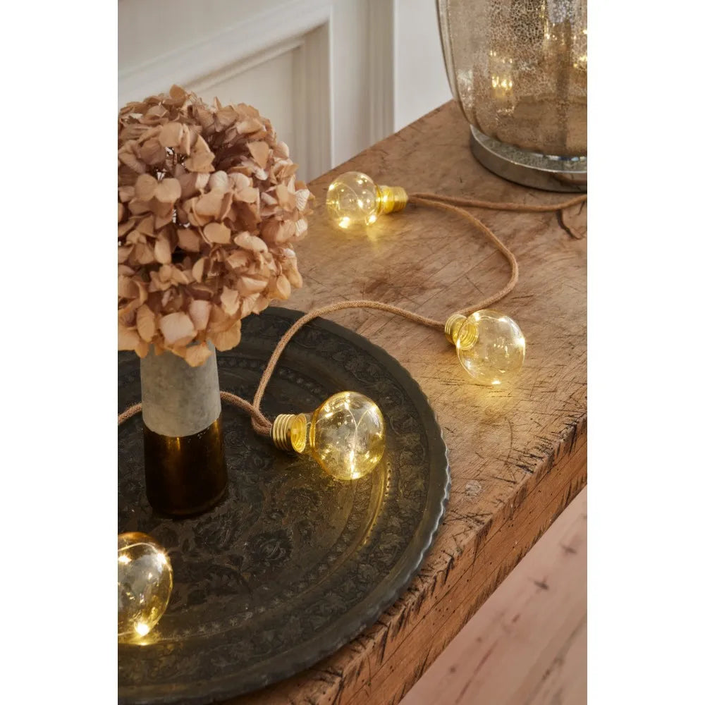 String of warm-toned LED globe lights with gold accents, strung on jute cord.