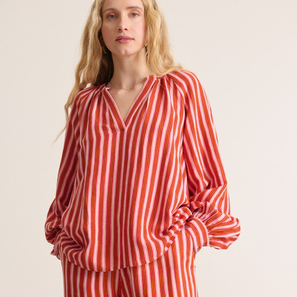Red, pink, and orange striped blouse with a V-neck and long, balloon sleeves.  Matching striped shorts are partially visible.