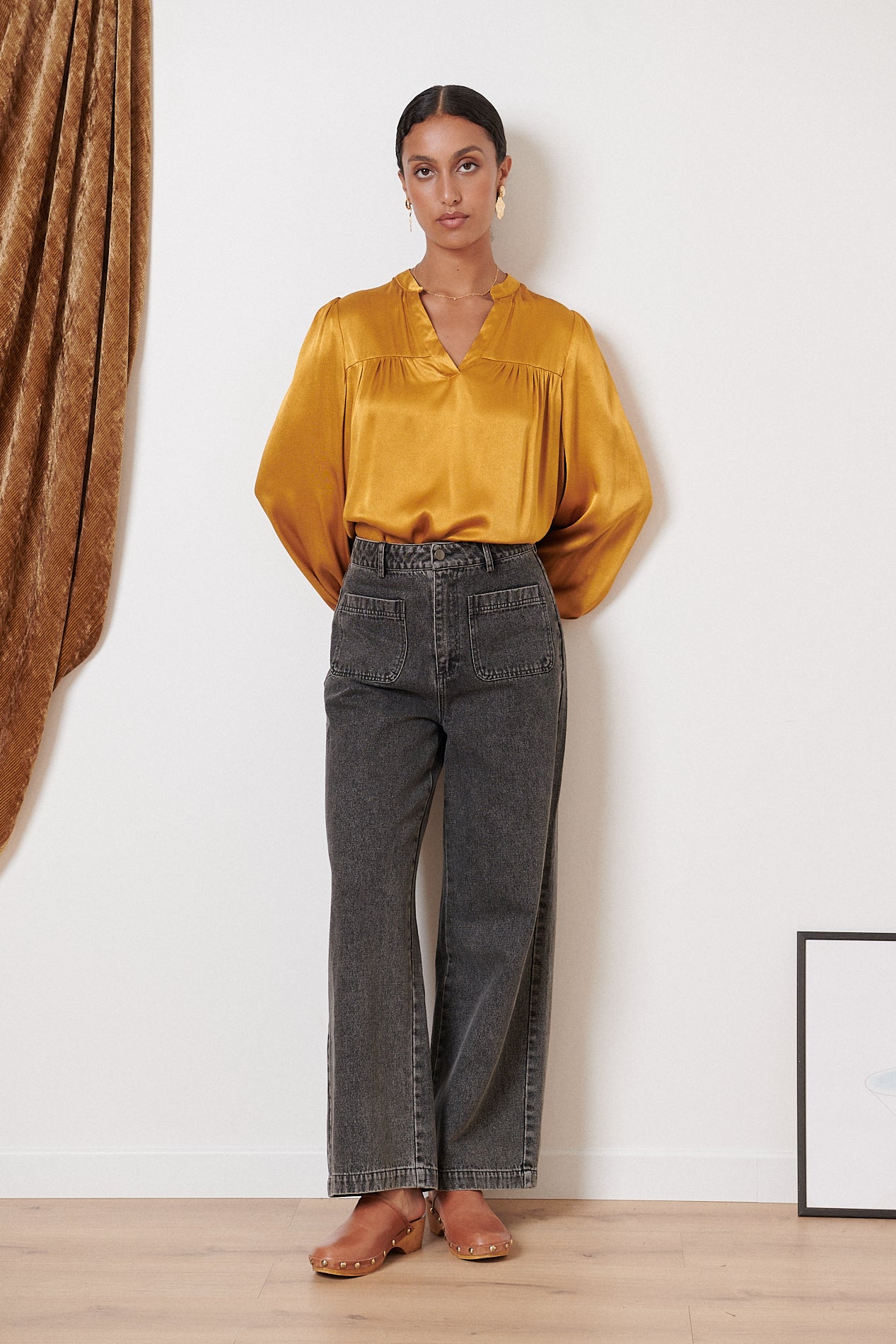 Mustard-colored satin blouse with a V-neck and long sleeves, paired with dark gray wide-leg jeans and light brown studded