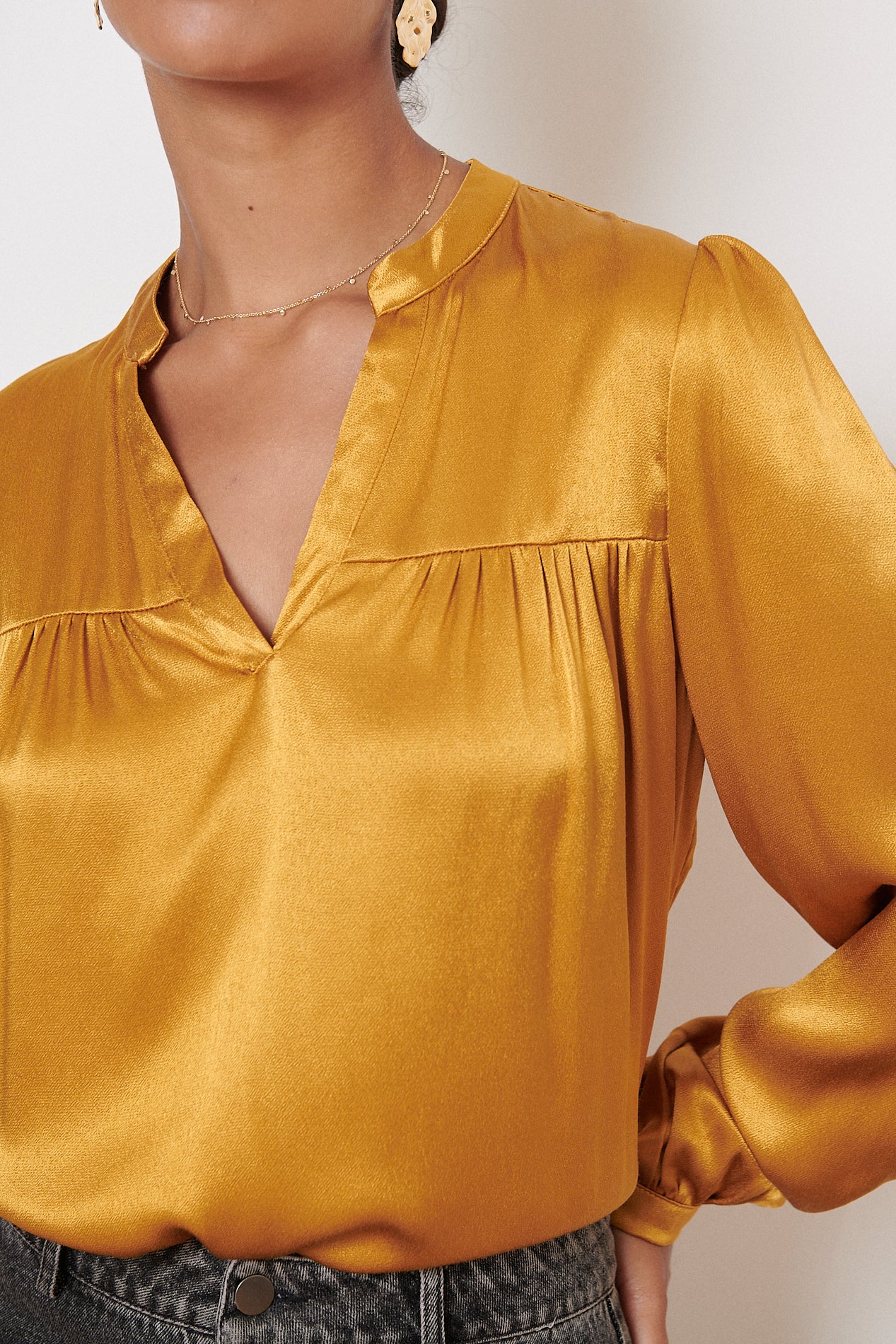 Mustard yellow satin blouse with a V-neck and long sleeves.  The blouse has subtle gathers at the chest.