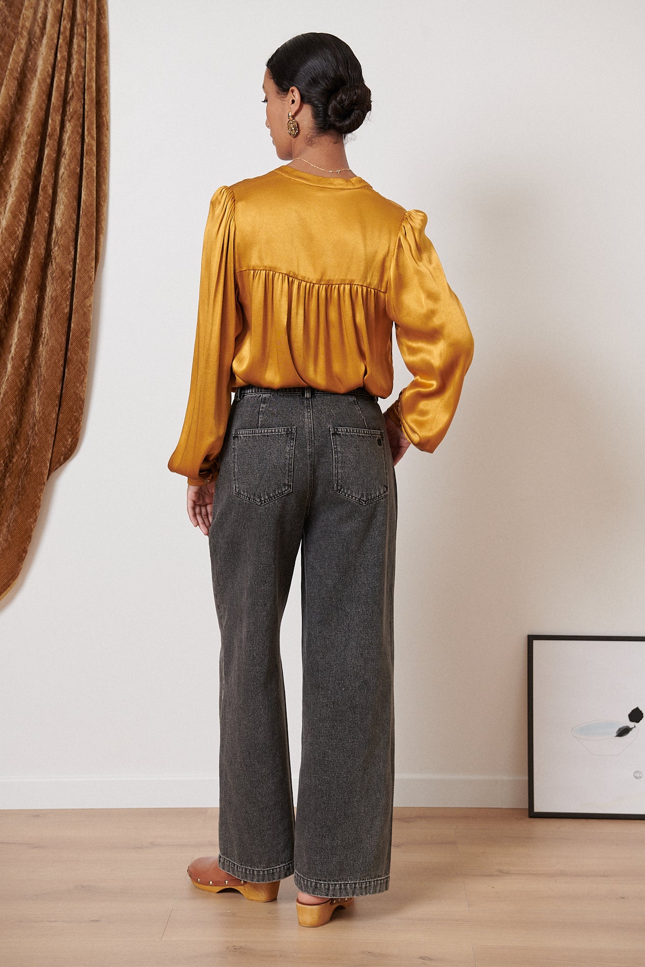 Woman's dark gray wide-leg jeans and mustard yellow satin blouse.  The blouse has long sleeves and a gathered bodice.