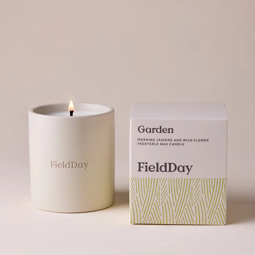 White candle with 'FieldDay' branding next to its packaging on a beige background
