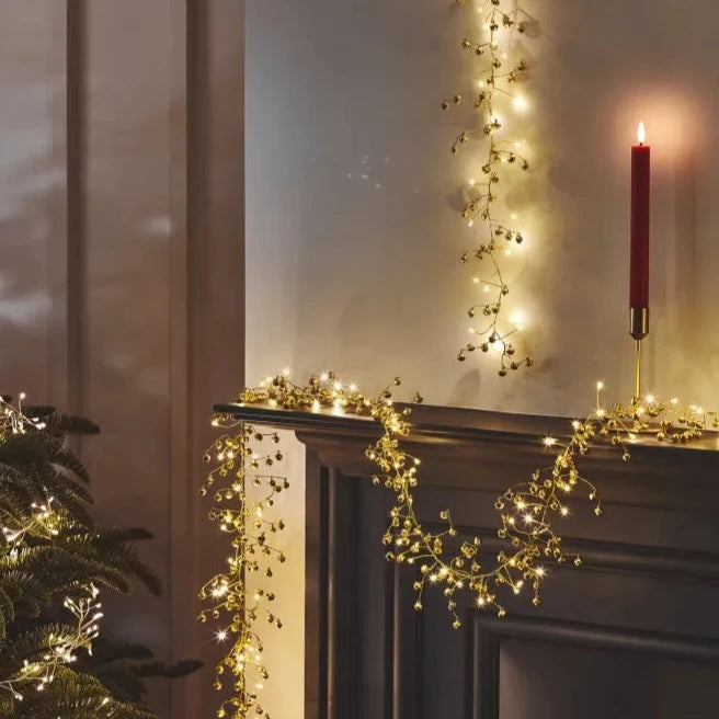 Gold bell and light garland draped across a mantelpiece.