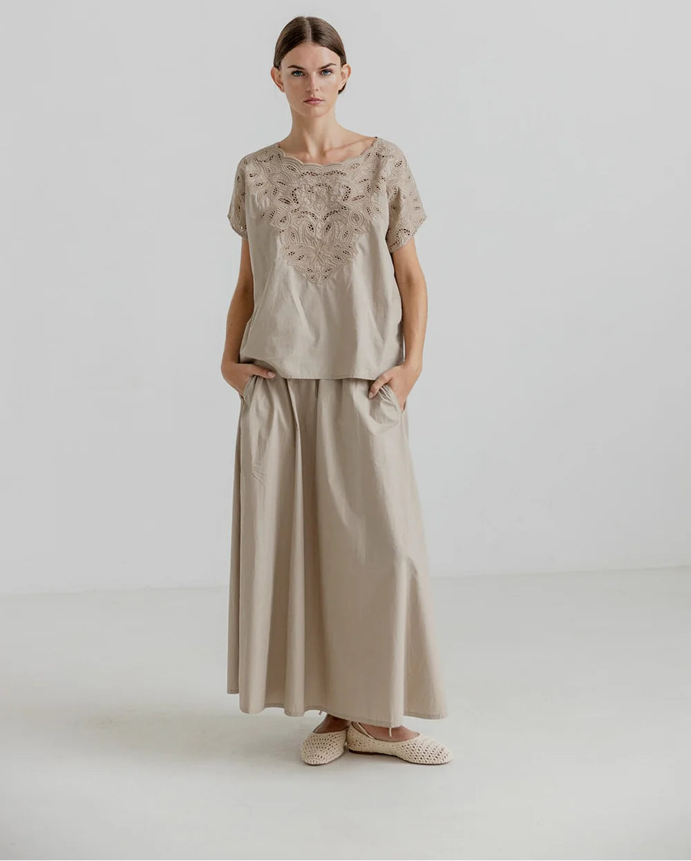 Woman wearing a beige outfit with lace details on a white background