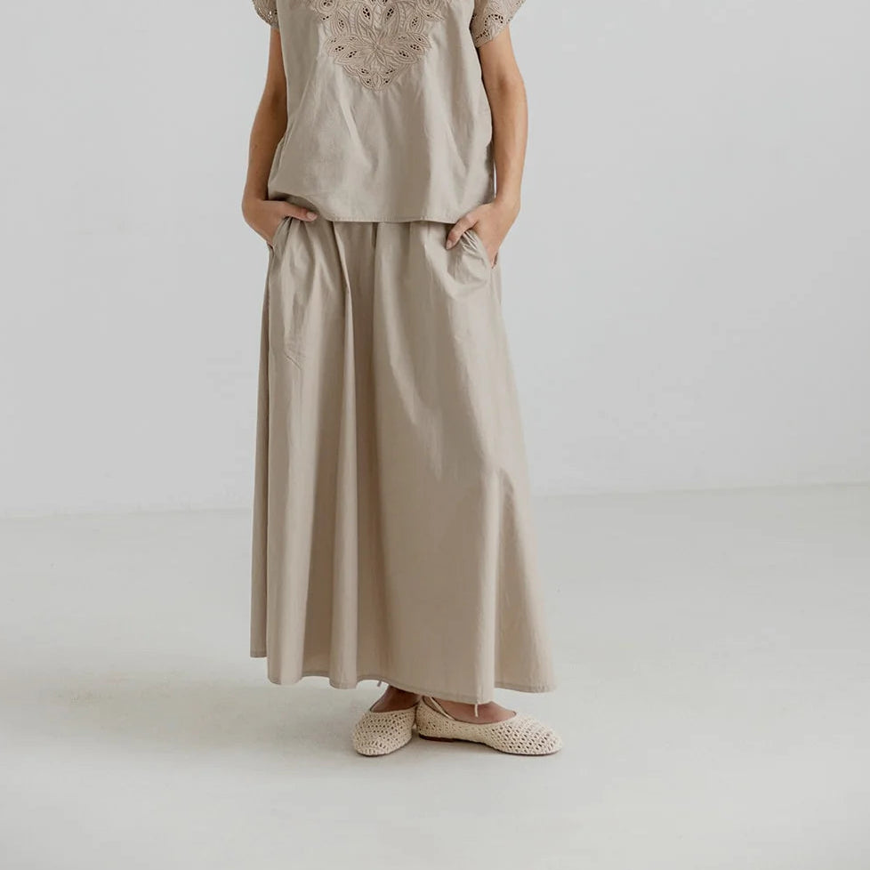 Woman wearing a beige outfit with lace top and wide-leg pants on a white background