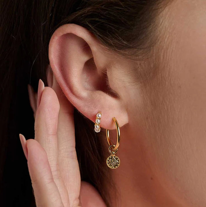 Gold hoop earring with a small round pendant worn by a person.