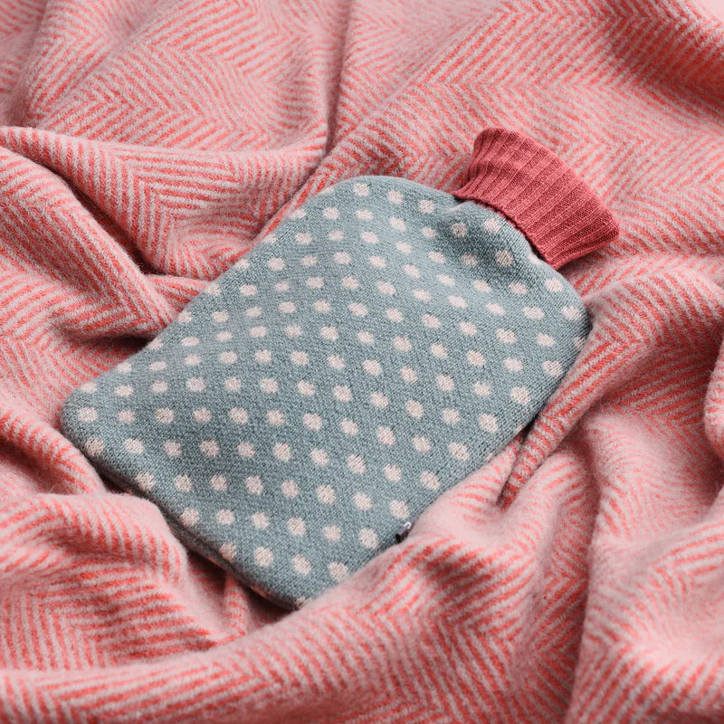 Teal knitted hot water bottle with white polka dots and a pink ribbed neck.