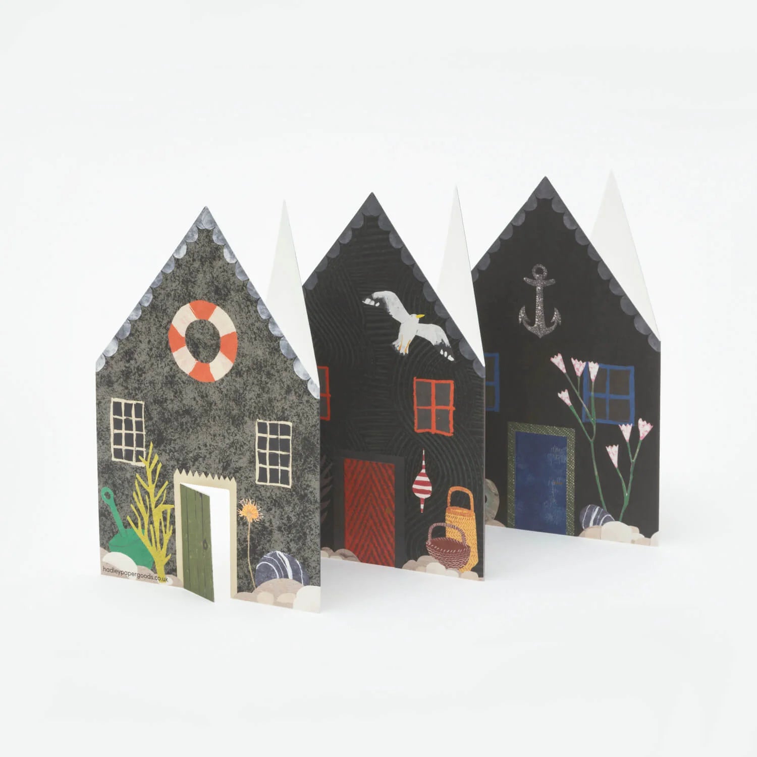 Three illustrated paper houses, dark gray with various nautical and floral details, stand in a row.