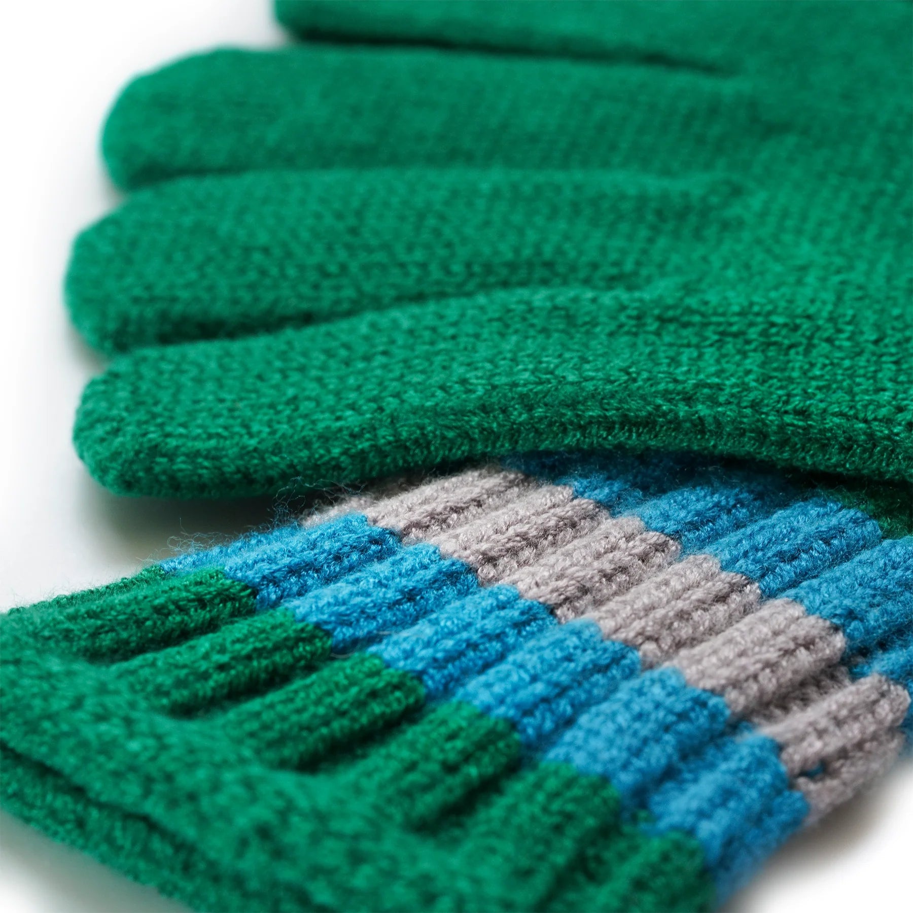 Close-up of a pair of green knitted gloves with teal, gray, and green striped cuffs.