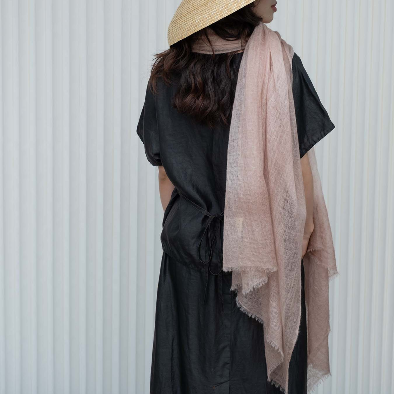 Person wearing a wide-brimmed hat and a light pink scarf against a white background