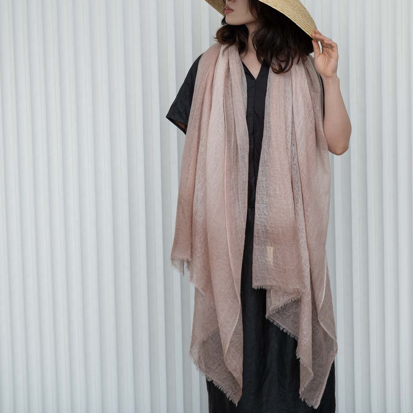 Person wearing a wide-brimmed hat and light pink scarf against a white background