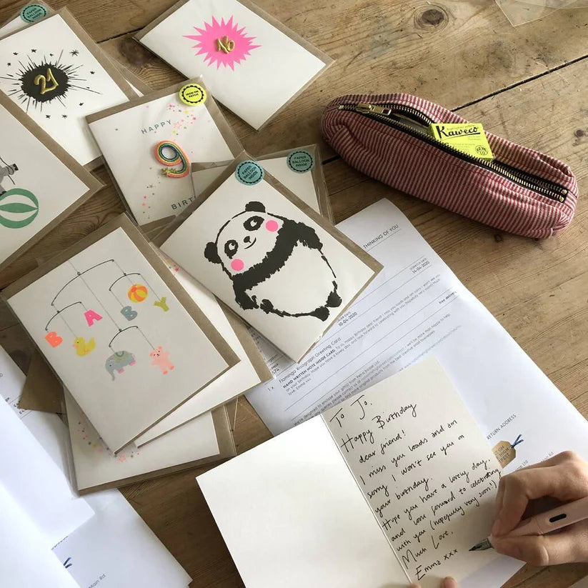Collection of greeting cards and a pen case on a wooden surface with a handwritten card.