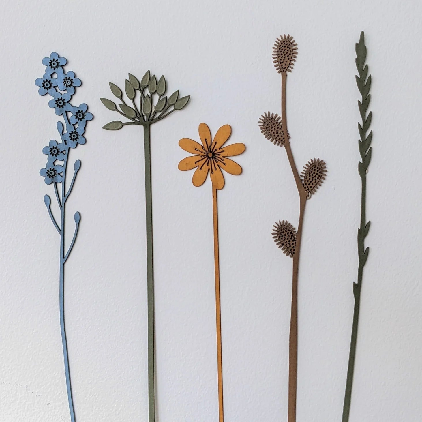 Five laser-cut wood floral designs in varying colors and styles.  Each features a slender stem and unique flower or foliage.