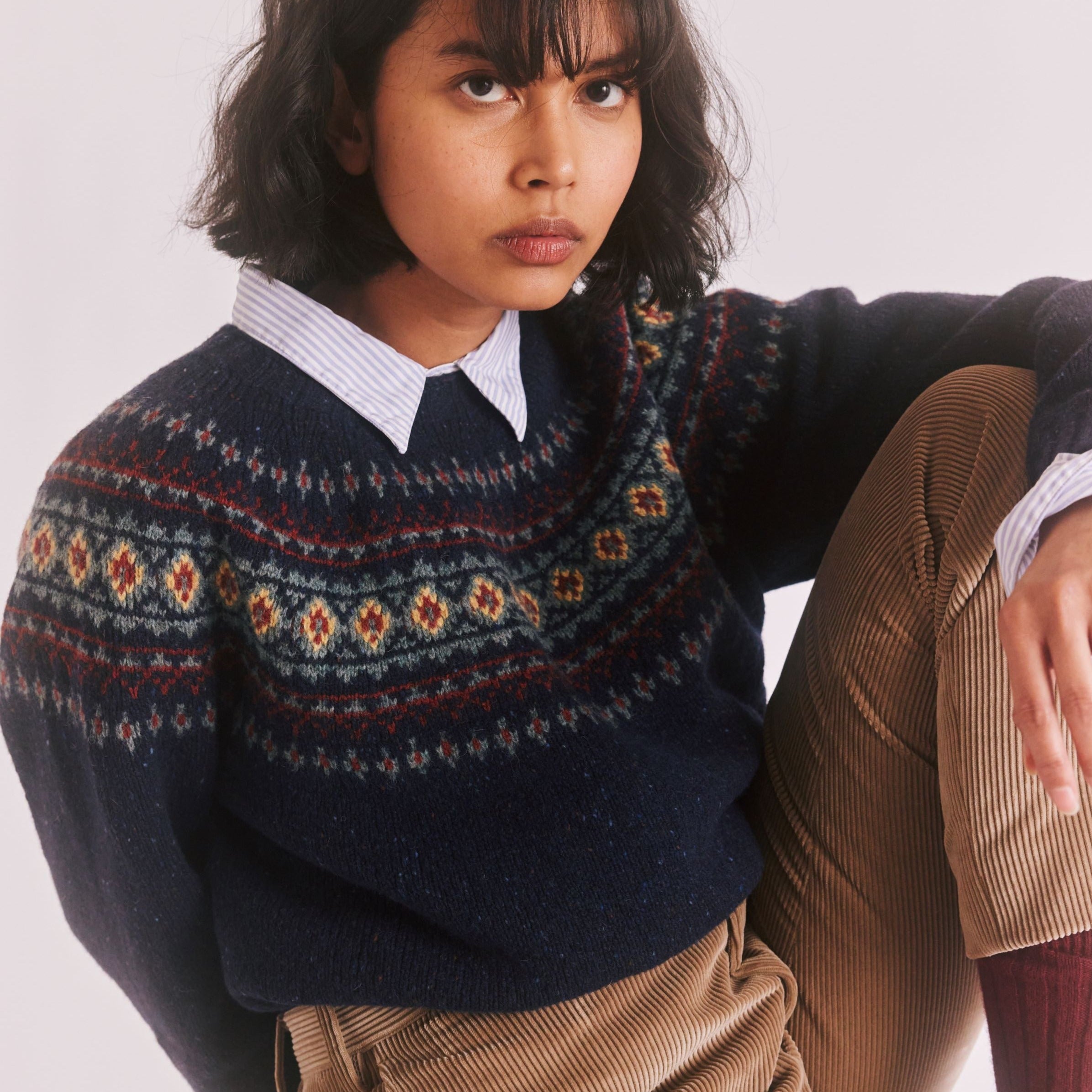 Dark navy blue crewneck sweater with a Fair Isle-style pattern in muted reds, greens, and yellows.