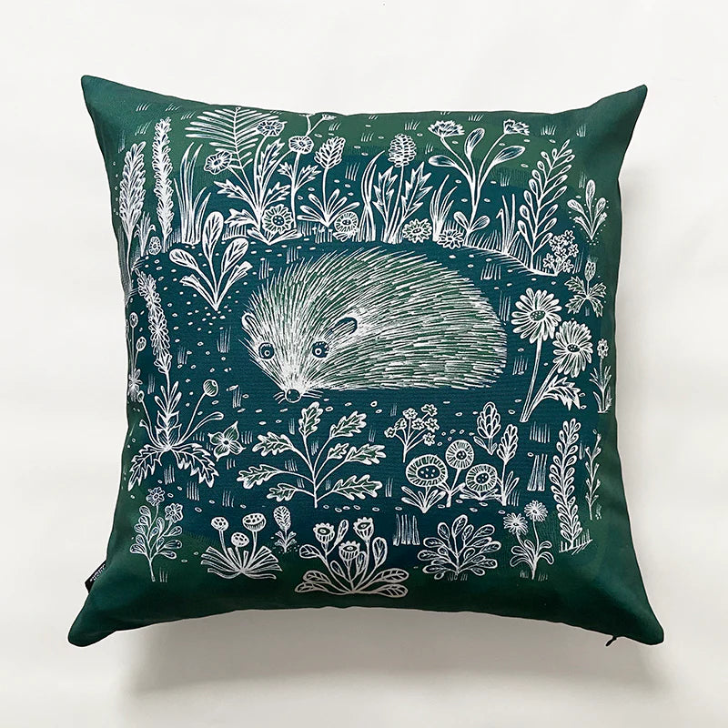 Dark green cushion featuring a white line drawing of a hedgehog amongst wildflowers.