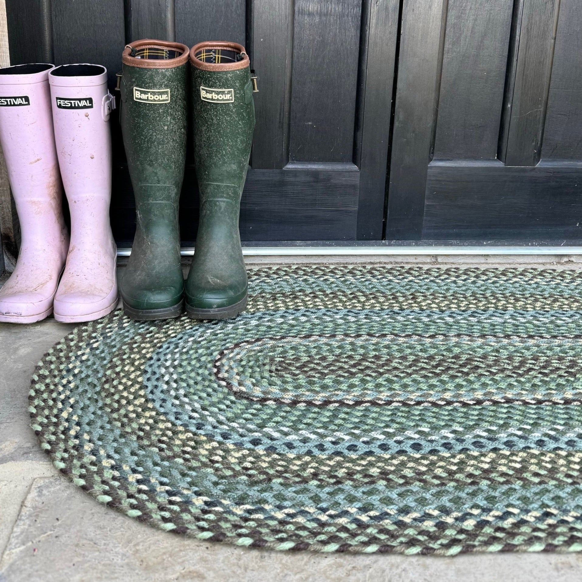 Green and pink boots on a braided mat outside a wooden door.