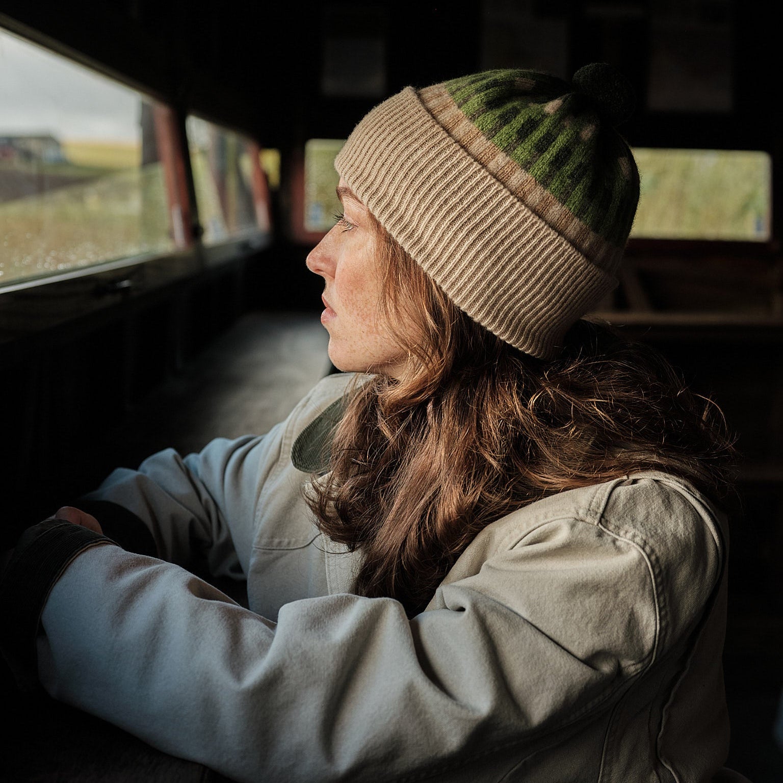 Person wearing a patterned beanie and jacket sitting inside a vehicle with a scenic view outside.